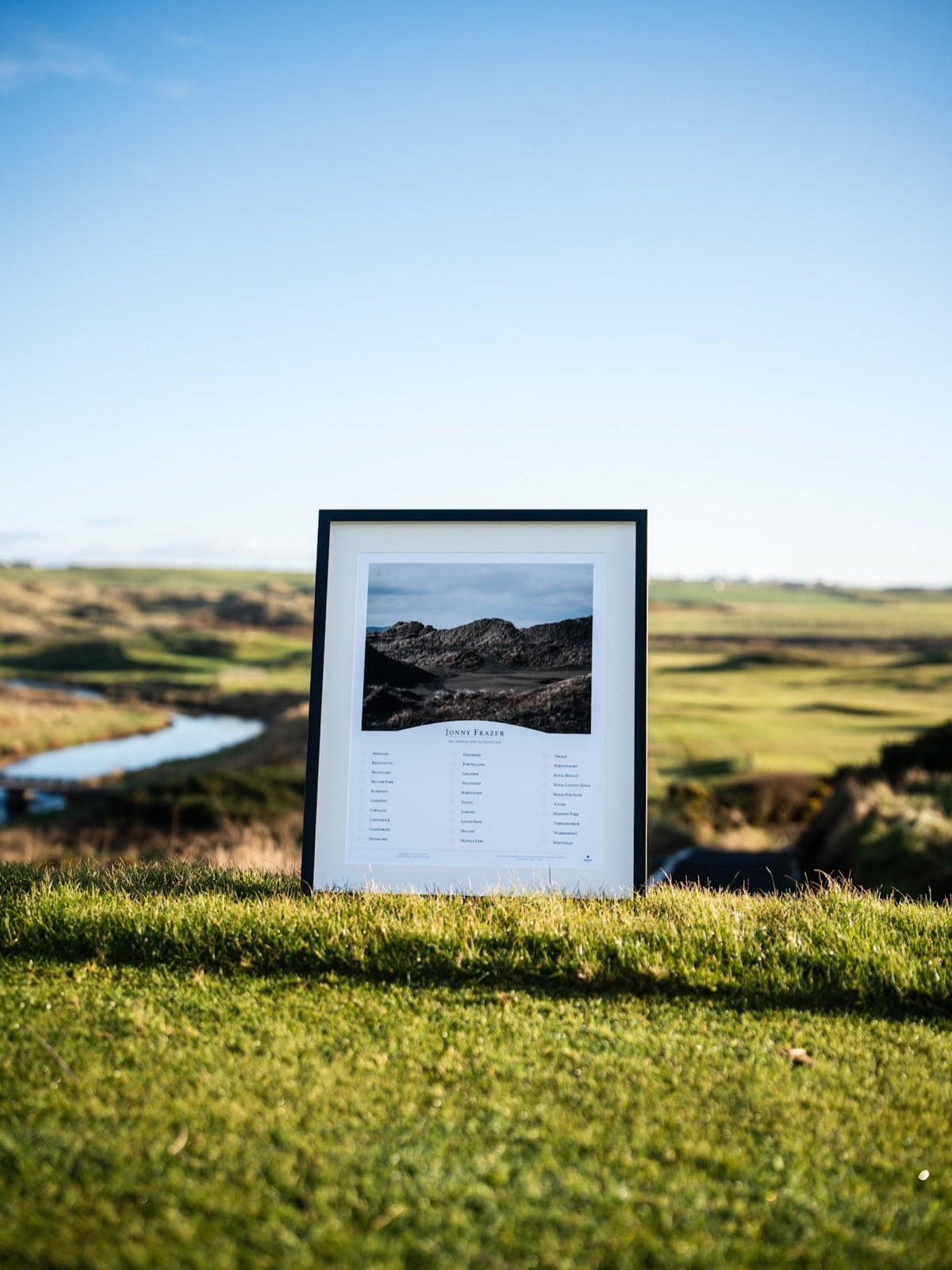 A framed BHÍOS photography piece standing on the turf at Portstewart, the links running away behind it.